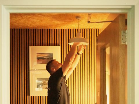 An electrician fitting a pendant light in a room with slatted timber walls